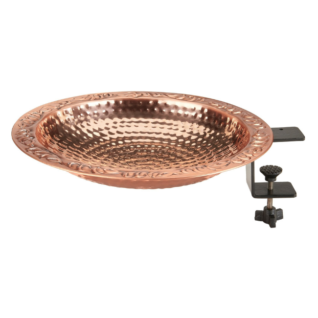 A scenic view of the hammered copper birdbath securely attached to a white deck railing, surrounded by lush green plants.