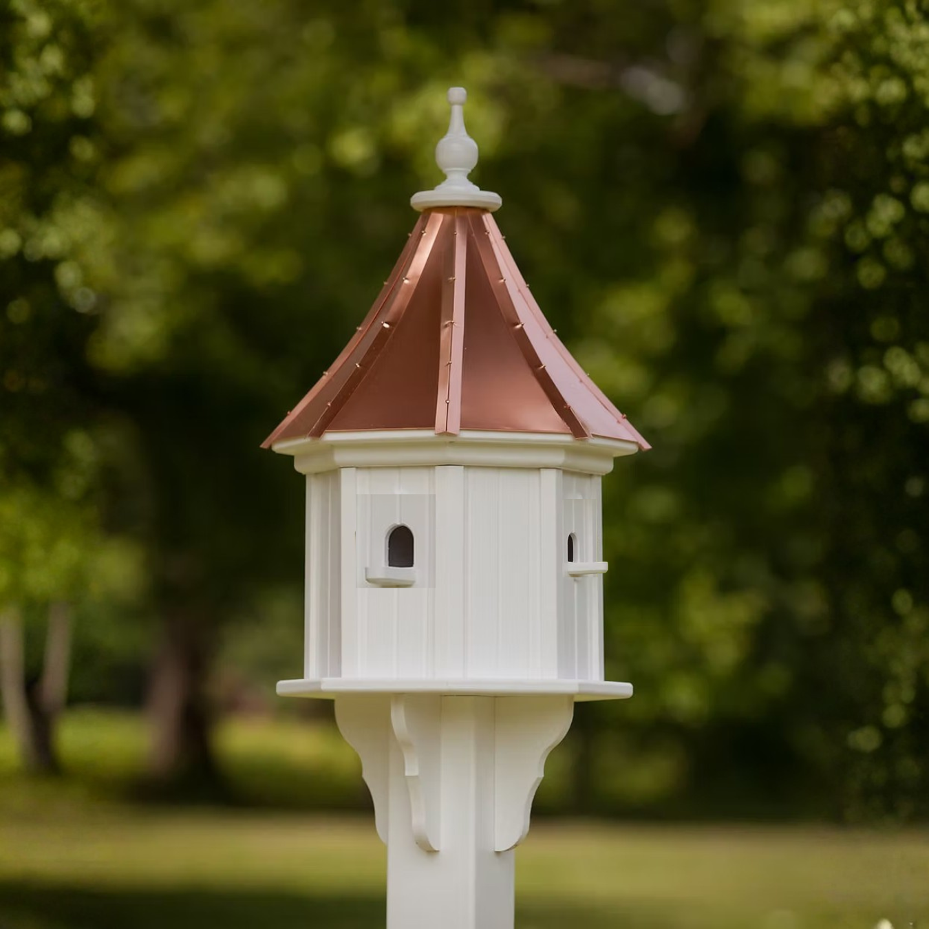 Decorative white birdhouse with a sloped copper roof against a green outdoor background