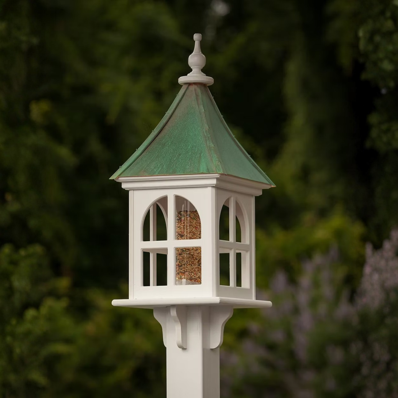 White bird feeder with windows and a  patina copper roof against a blurred natural background